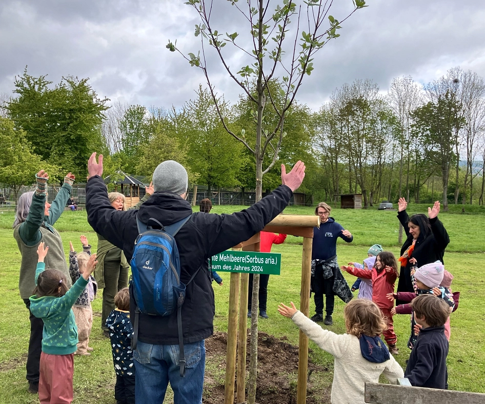 Kinder tanzen um den neu gepflanzten Baum und singen ein Lied